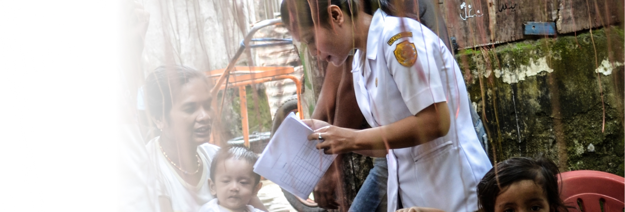 A female health worker is collecting data from a mother holding a child